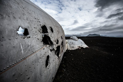 Abandoned military airplane at beach against cloudy sky