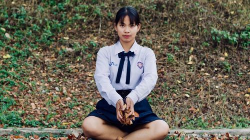 Portrait of woman holding leaves while sitting on field