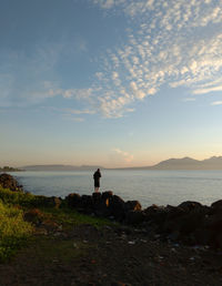 Rear view of man standing at beach against sky during sunset