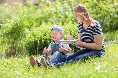 Mother feeding food to son in lawn on sunny day