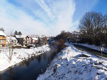 Snow covered houses by canal against sky