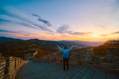 Rear view of man with arms outstretched standing on steps at great wall of china during sunset