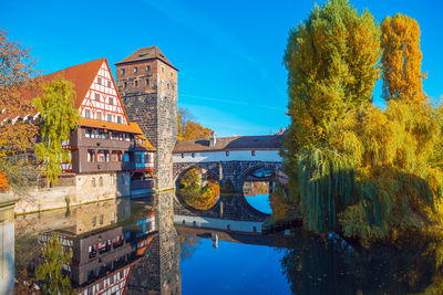 Arch bridge over river amidst buildings against blue sky