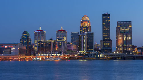 Illuminated buildings in city against sky at dusk