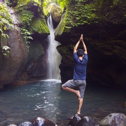 Rear view of man doing yoga against waterfall