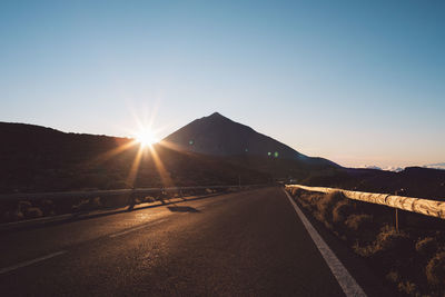 Road leading towards mountains against clear sky during sunset