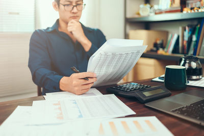 Midsection of man holding paper while sitting on table