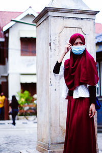 Woman wearing mask in hijab standing against building in city