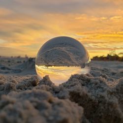 Close-up of crystal ball on beach against sky during sunset