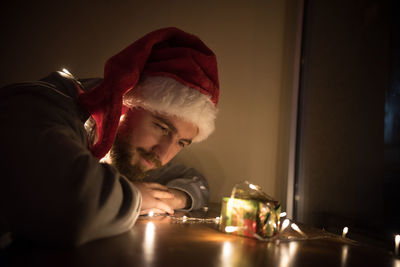 Close-up of young man by illuminated christmas lights on gift in darkroom