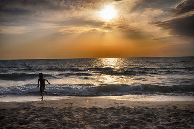 Silhouette boy running at beach against cloudy sky during sunset