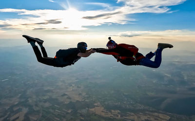 Two people holding hands during free fall skydive jump against sunset in the sky. 