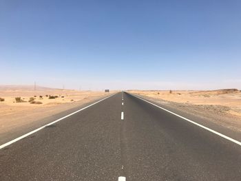 Road passing through desert against clear sky