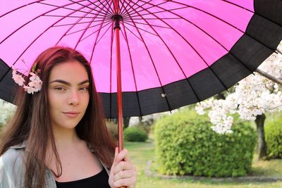 Portrait of teenage girl holding pink umbrella at park