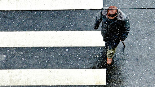 High angle view of man crossing road in city during snowfall