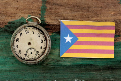 Close-up of damaged pocket watch by catalonia flag on table