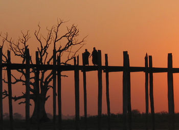 Silhouette birds perching on wooden post against sky during sunset