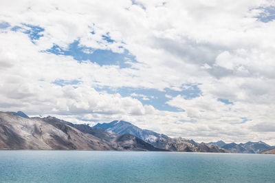 Scenic view of pangong lake by mountains against cloudy sky