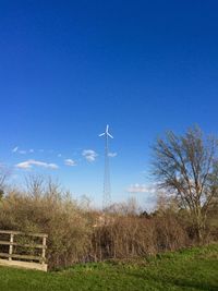 Low angle view of wind turbines on field against blue sky