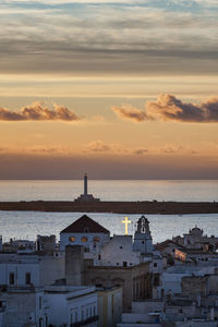 Buildings by sea against sky during sunset