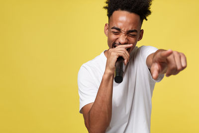 Young man looking away while standing against yellow background