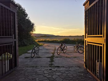 Bicycle on footpath by buildings against sky during sunset