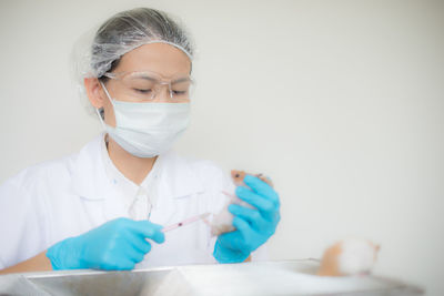 Doctor giving injection to rat against white background