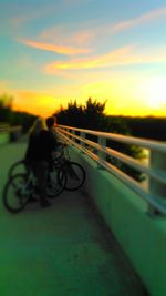 Silhouette man riding bicycle on road against sky during sunset
