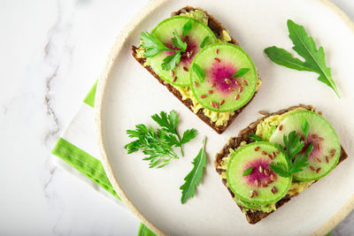 Homemade toasts with organic watemelon radish, avocado and flex seeds on white marble background.