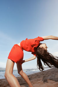 Rear view of woman exercising at beach against clear sky