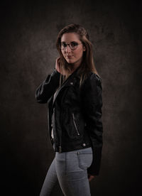 Portrait of young woman standing against black background