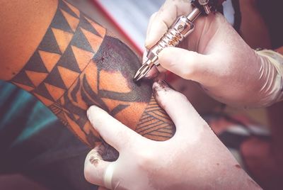 Cropped hand making tattoo on man