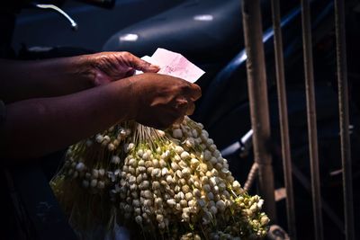 Cropped hands of woman holding banknote with floral garland