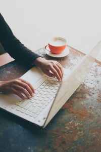 Close-up of woman hands using laptop by coffee cup on table