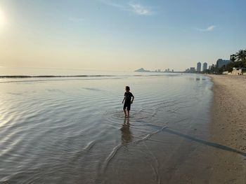 Rear view of woman walking at beach against sky during sunset