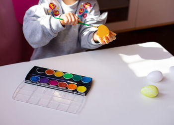 Close up of childrens hands holding easter egg and painting with brush at home. preparing for easter