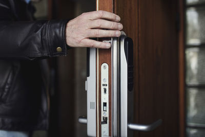 Cropped image of senior man wearing leather jacket opening wooden door