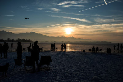 Silhouette people at beach against sky during sunset