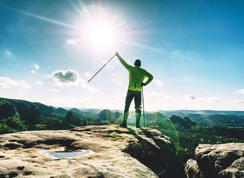 Funny slim blond tourist guy holds trekking stick on rocky top. man in yellow black spoert jersey