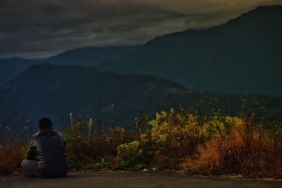 Rear view of man sitting on mountain against sky