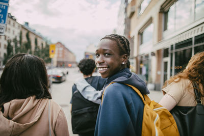 Portrait of smiling teenage boy looking over shoulder while walking with friends in city street