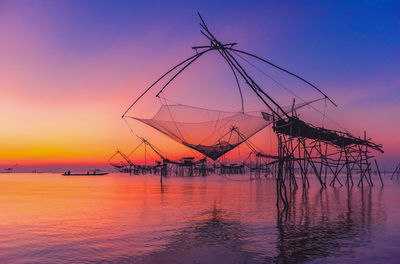 Silhouette fishing net by sea against sky during sunset
