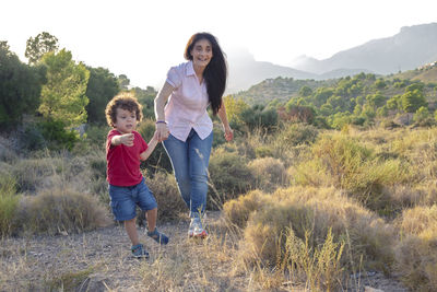 Mother and son playing jogging in the field on a day out holding hands and laughing