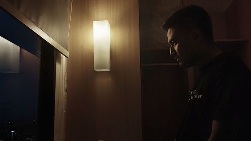 Side view of young man looking at illuminated lamp at home