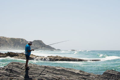 Man fishing by sea against clear sky