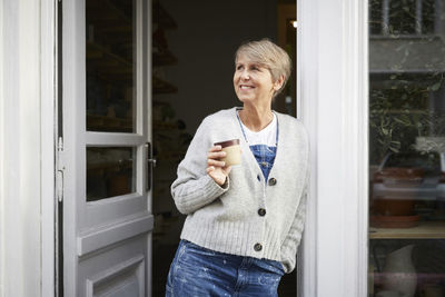 Smiling mature woman having coffee at entrance of art studio