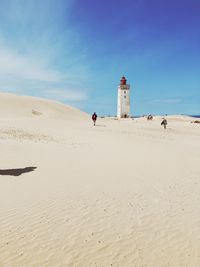 View of lighthouse at beach against blue sky during sunny day