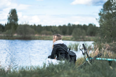 Rear view of woman sitting on grass against sky