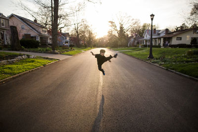 Full length of playful boy kicking in air while practicing karate on road during sunset