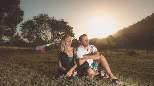 Couple sitting on grass in park at sunset